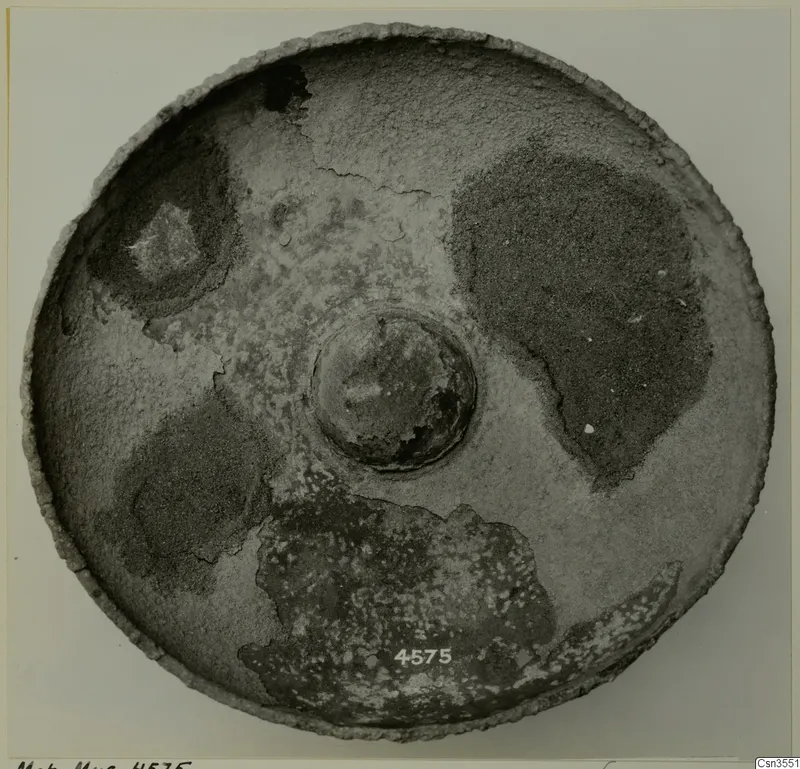 Round bowl seen from above, with a raised central boss and a mottled, worn surface