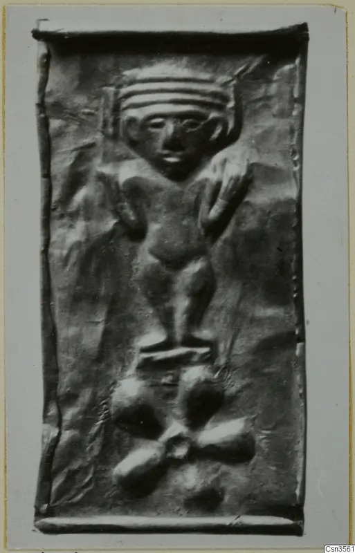 Embossed metal plaque with a standing figure wearing a banded headdress, above a cluster of rounded lobed shapes.