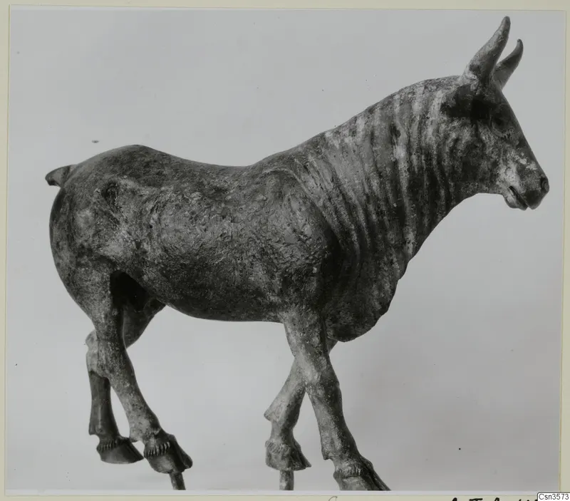 Bronze figure of a horned animal standing in profile, facing right, with four legs and hooves
