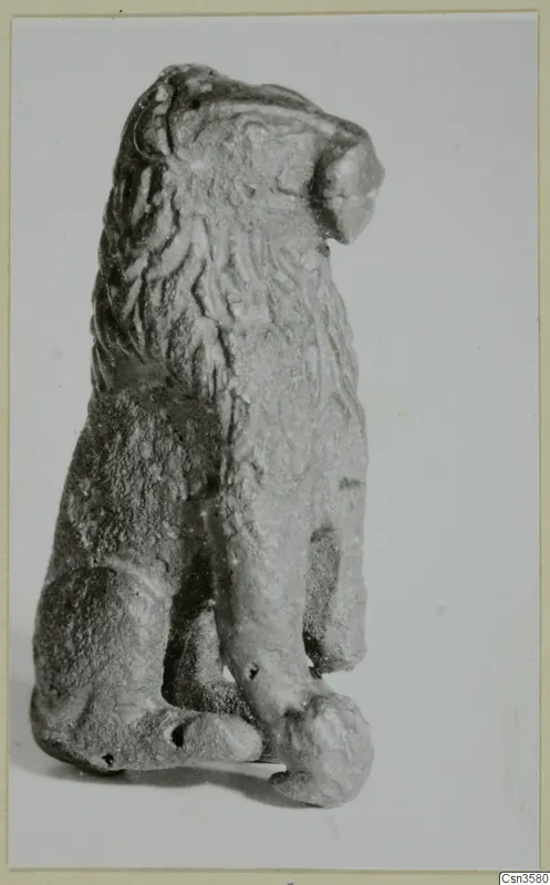 Small bronze figure of a seated animal with a mane, shown from a side view against a plain background