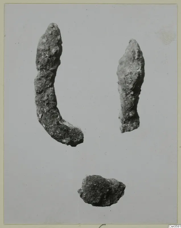 Three corroded metal pieces on a pale background: two elongated fragments and a small irregular lump.