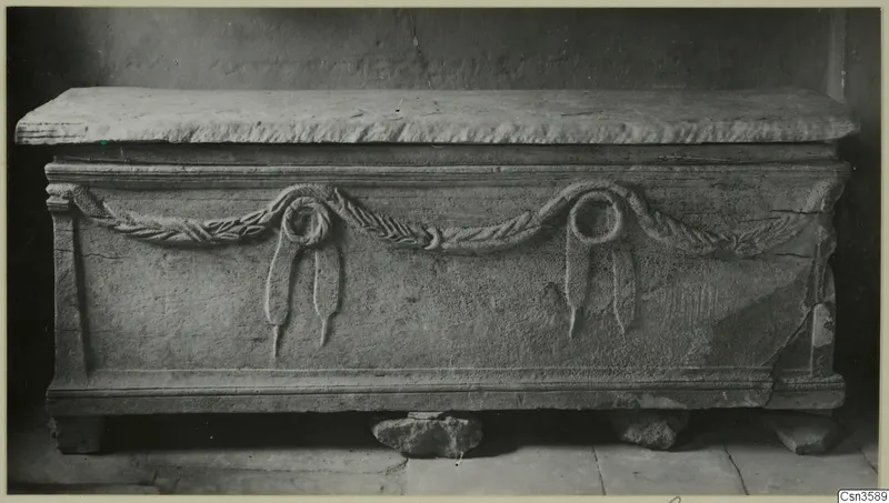 Stone sarcophagus with a carved garland and two knotted ribbons across its front panel