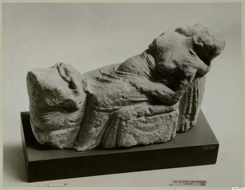 Carved limestone sculpture of a reclining draped figure with head resting on one arm, on a dark stand