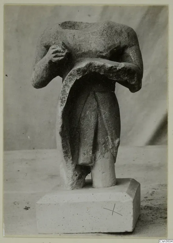 Headless limestone figurine of a standing figure with arms across the chest, on a rectangular base.