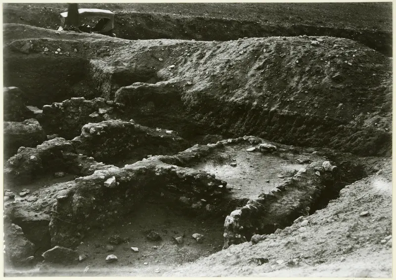 Excavation trench with exposed stone walls and rubble, with a partly visible person at the top left edge