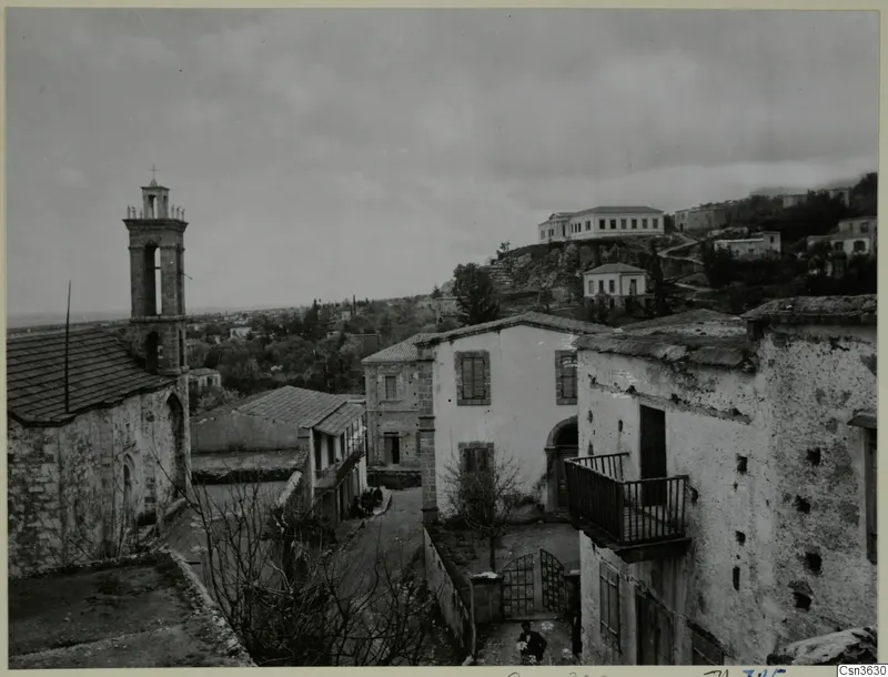Village street at Lapithos with a church bell tower, whitewashed and stone houses, and bare trees.