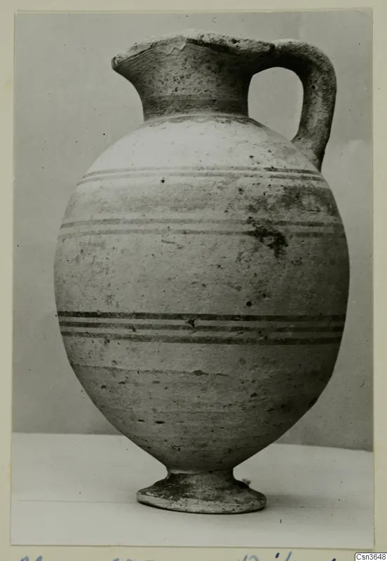Pottery jug with a single handle, a tall neck and horizontal dark bands on a pale body, on a stand.