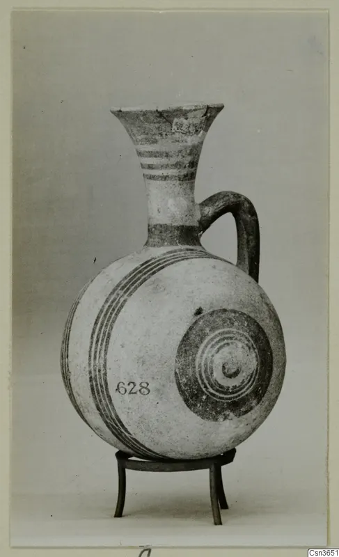Painted pottery juglet with a flaring neck and single loop handle, standing on a metal tripod stand.