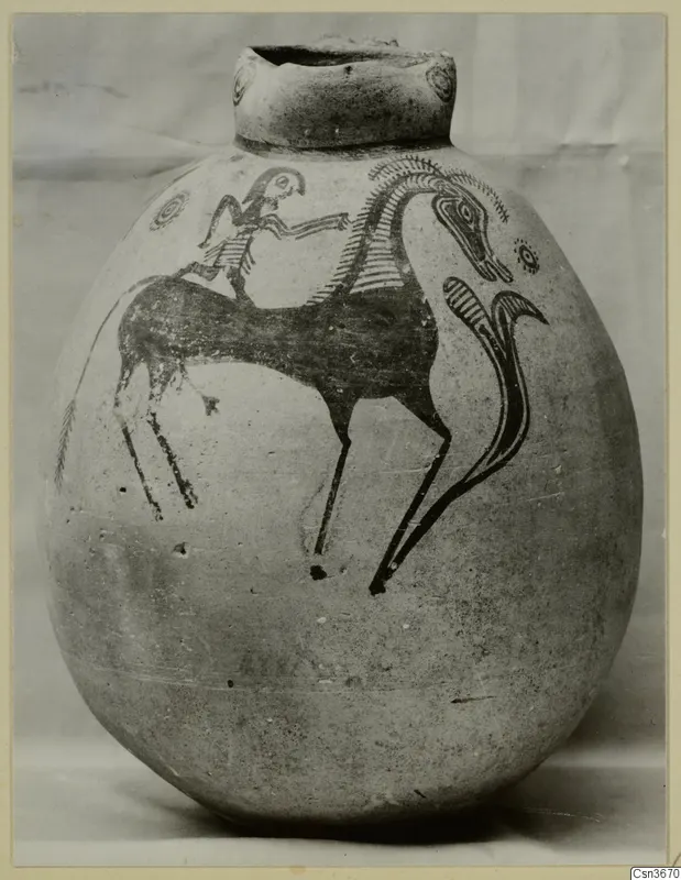 Round painted jug with a dark figure seated on a long-necked animal, photographed against a pale backdrop.