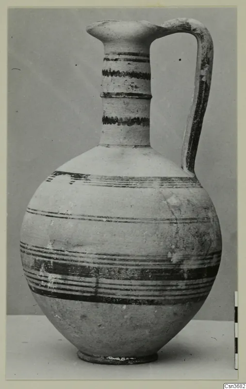 Bichrome IV jug with dark painted bands, a strap handle and a pinched spout, against a grey backdrop