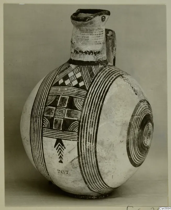 Painted pottery jug with a tall neck, a side loop handle and bands of dark concentric and geometric patterns on a pale body.
