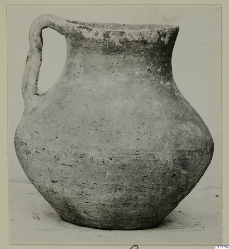 Pottery jug with a single loop handle, seen from the side against a plain light background