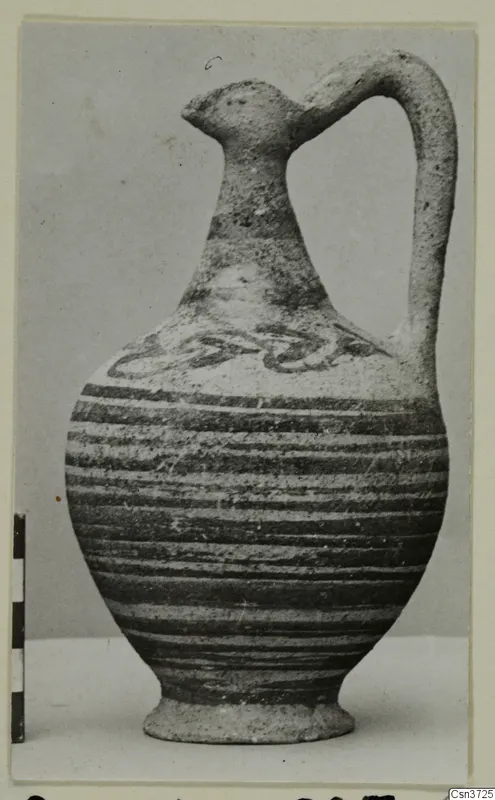 Painted pottery jug with a bird-head spout and strap handle, beside a scale bar