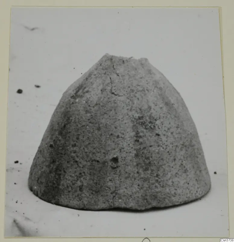 Grey, rough-surfaced dome-shaped object with a broken flat top, photographed alone on a pale background