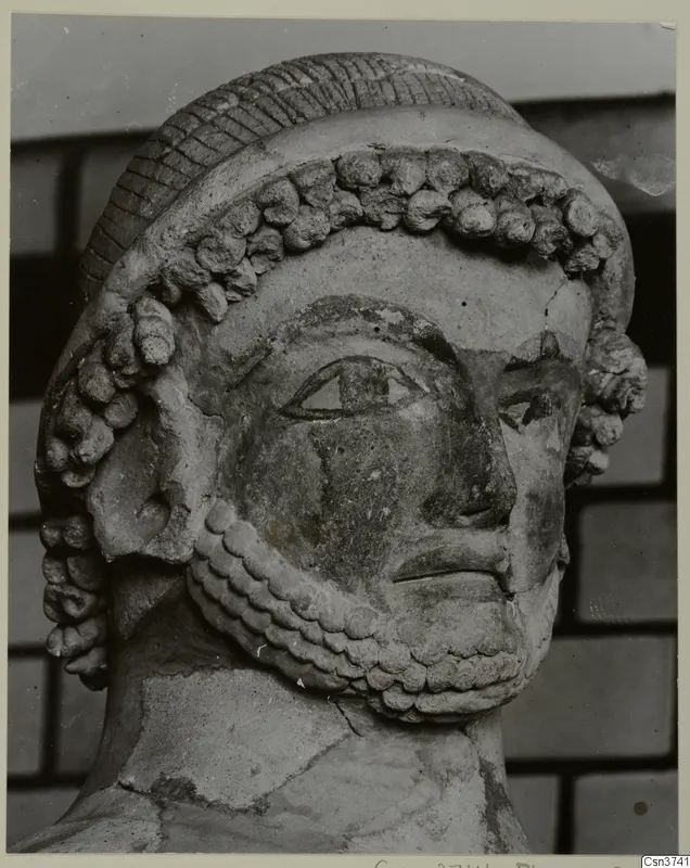 Close-up of a sculpted head with a ridged cap, rows of curled locks and a curled beard, Terracotta Cypro-Greek II