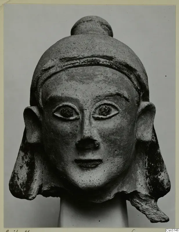 Terracotta head with a tall rounded cap, large projecting ears and flaring side locks, shown on a plain support