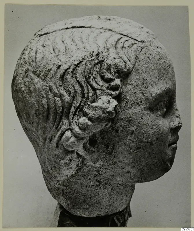 Carved stone head from Mersinaki, shown in profile facing right, with wavy hair and rounded curls above the ear.