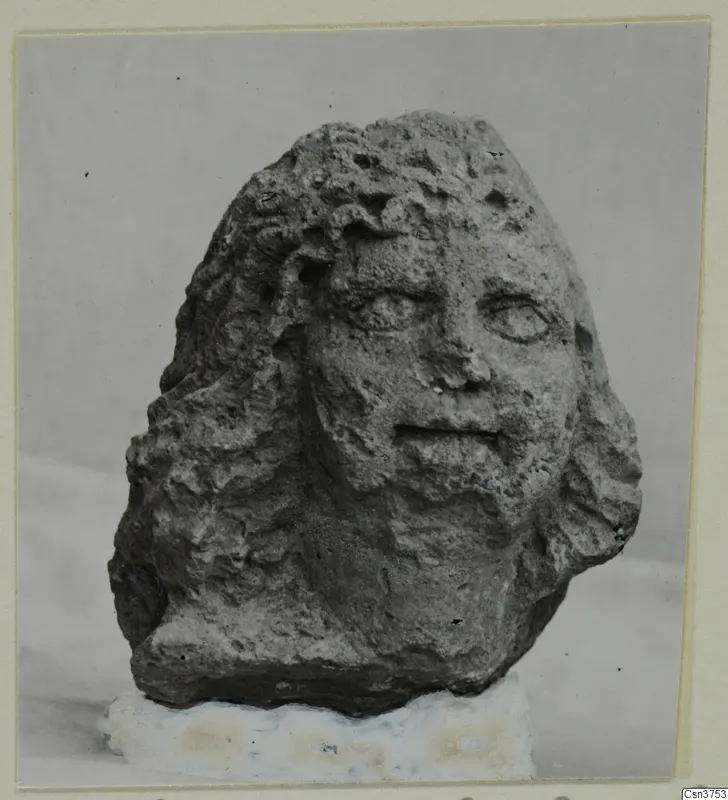 Stone head from Soli with wavy hair and worn facial features, on a white base.