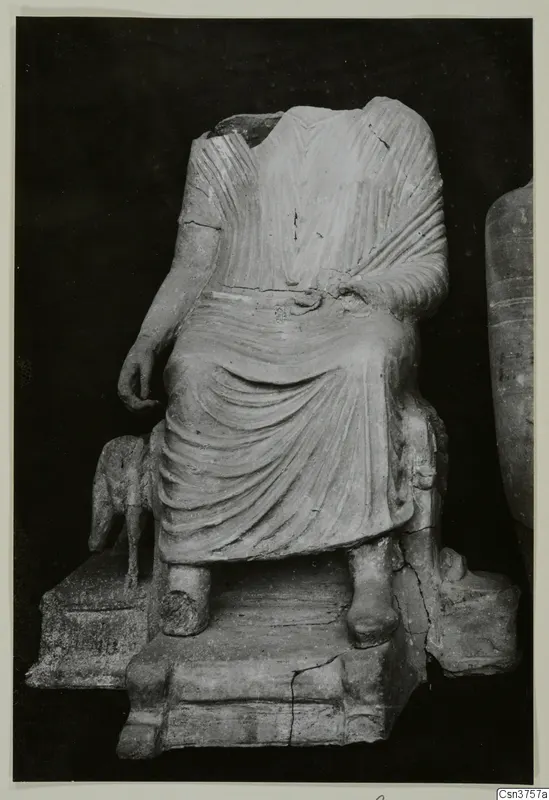 Headless seated figure in a draped garment on a stepped base, with a small animal figure at its left side.