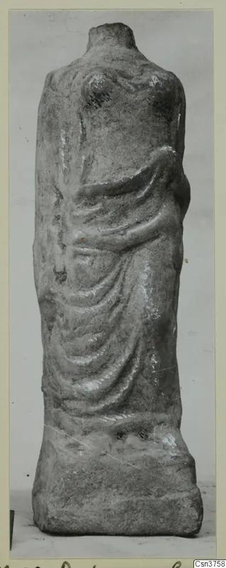 Headless draped statue fragment of grey stone standing on a rectangular base