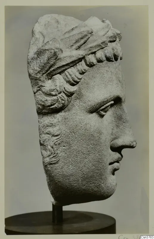 Carved stone head of a figure in profile facing right, with layered hair bands, on a dark stand.