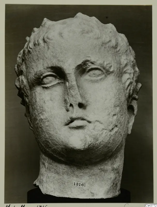 Roman sculpture: pale stone head with short curled hair, photographed from the front against a dark backdrop