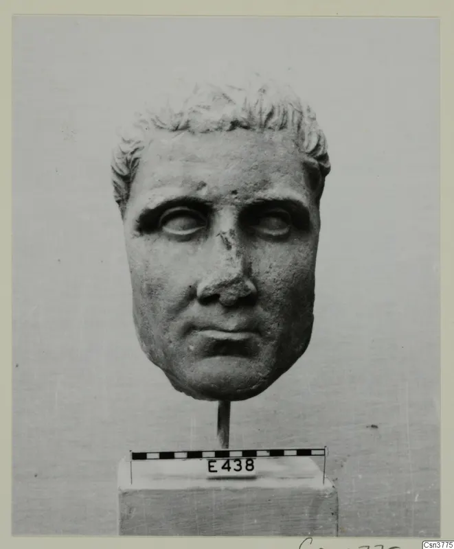 Roman sculpture: stone head of a man with short curled hair, mounted on a rod above a base with a scale bar.
