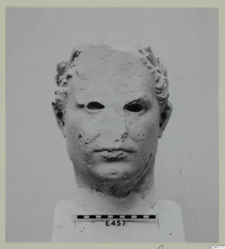 Marble head of a male figure with curled hair, eyes hollowed out, mounted on a plinth