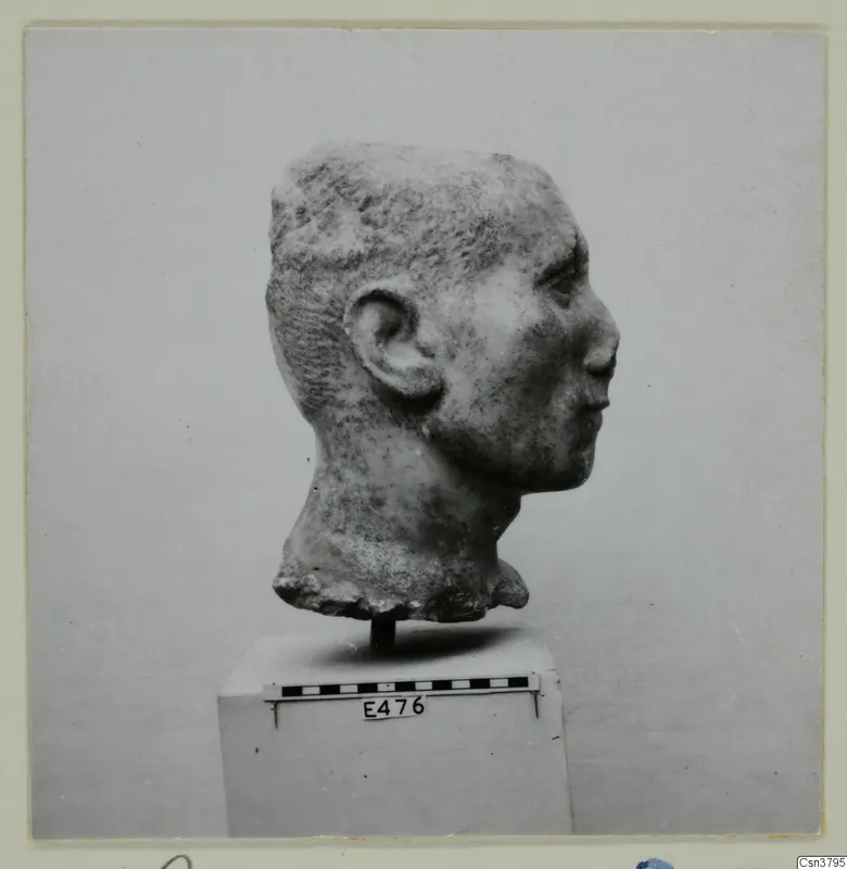 Stone head of a figure in profile, set on a pedestal beside a scale bar.