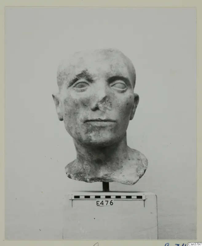 Roman stone sculpture of a man's head with a damaged nose, on a block with a scale bar