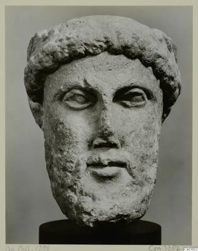 Carved stone head of a bearded man with short curly hair, shown on a dark cylindrical base.