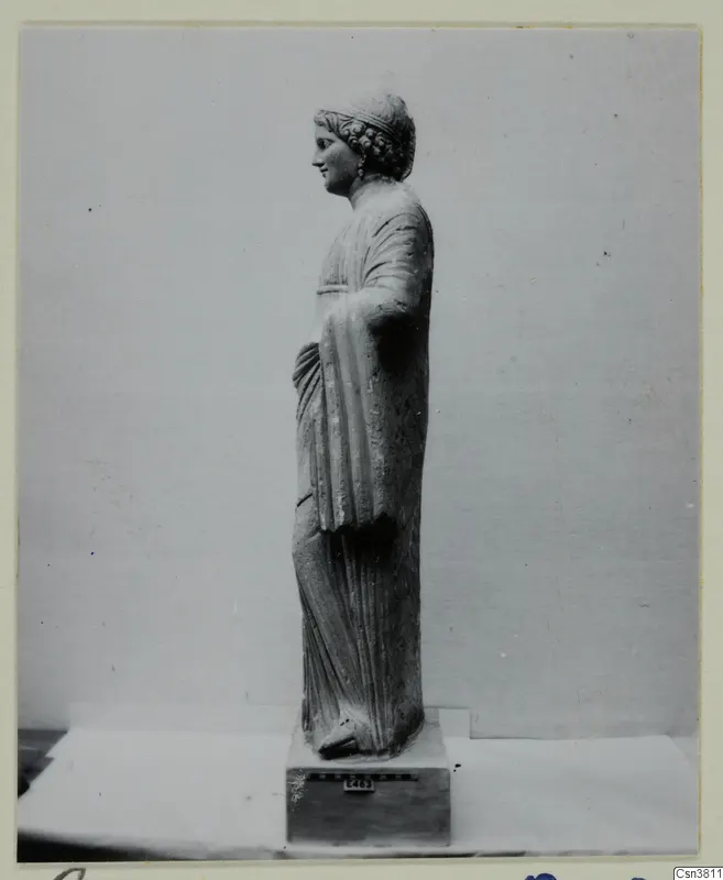 Standing stone statue of a female figure, seen in profile facing left, on a square base