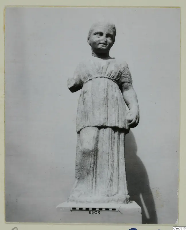 Stone statue of a standing figure in a short-sleeved belted tunic, on a plinth with a scale bar