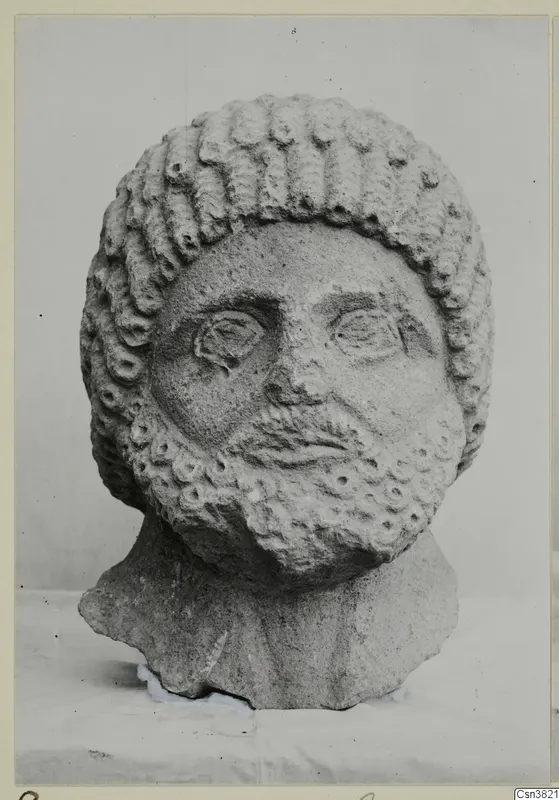 Carved stone head of a bearded man with rows of curls, shown in an old photograph mounted on a card