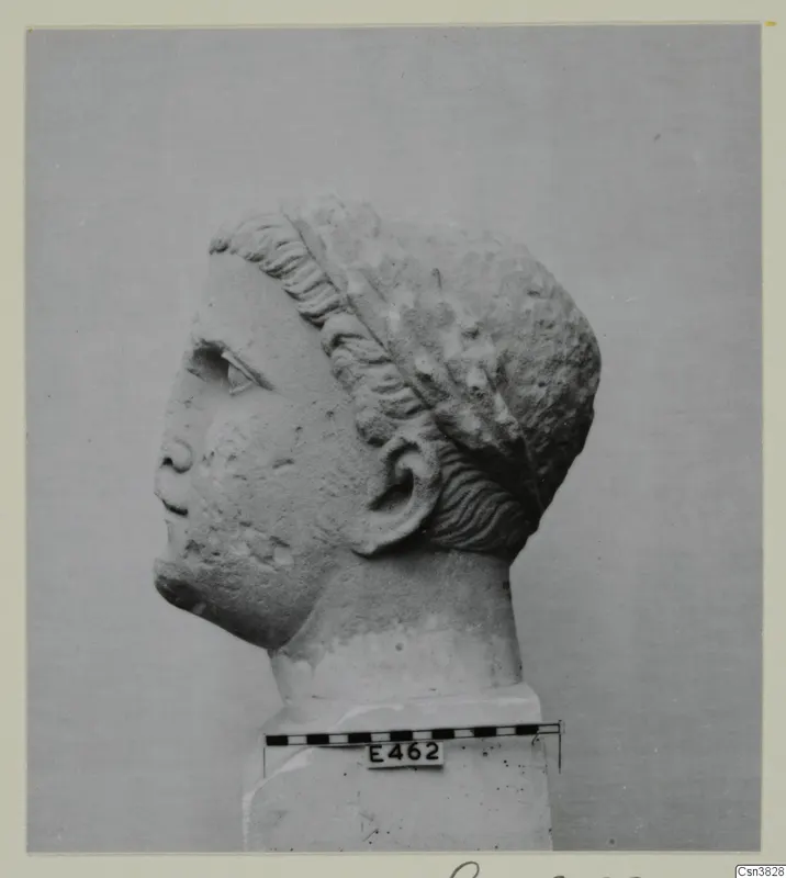 Stone head in profile facing left, with wavy hair swept back from the brow, on a block base beside a scale bar.