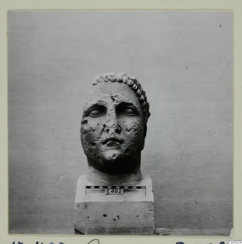 Stone head of a figure on a square plinth, with a scale bar and number label E462 fixed to the base
