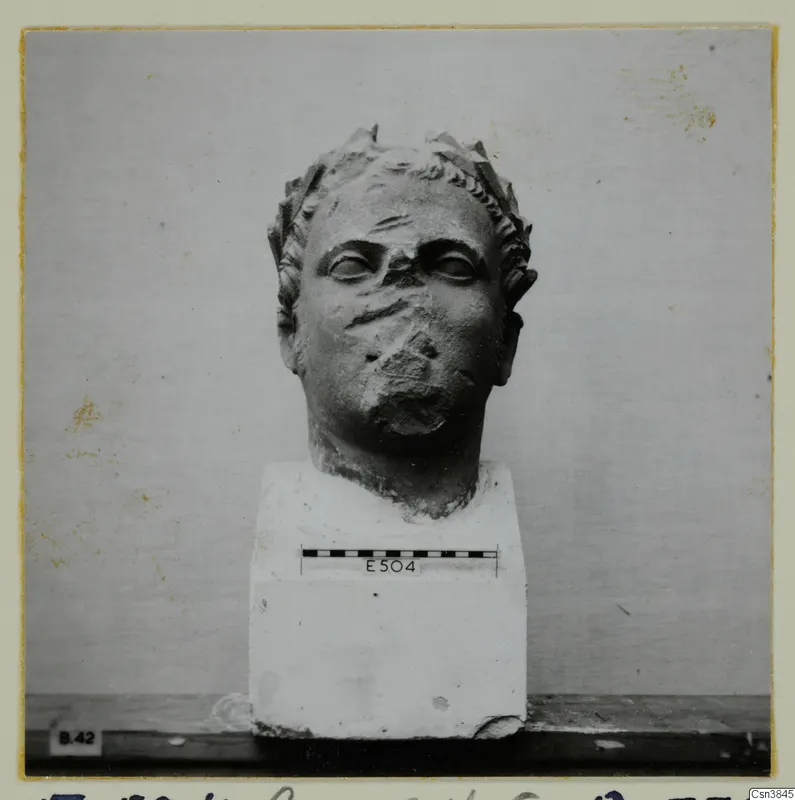 Carved stone head on a square block base, with a scale bar and number label E504 on the base