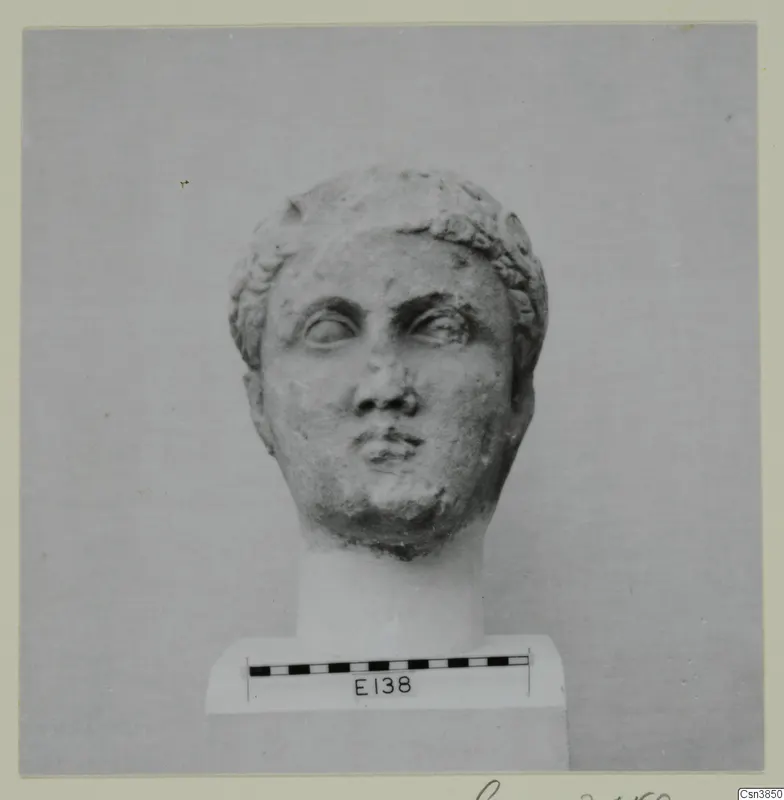Carved stone head with curled hair, set on a plinth beside a scale bar.