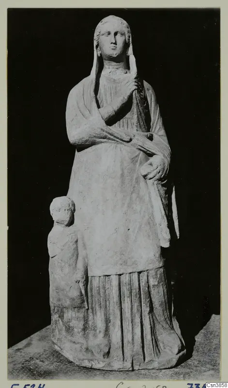 Standing draped female statue with a veil, with a small child figure at her side, photographed against a black background