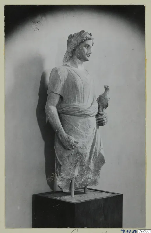 Stone statue of a standing male figure with a wreath in his hair, holding a small bird, on a dark wooden plinth