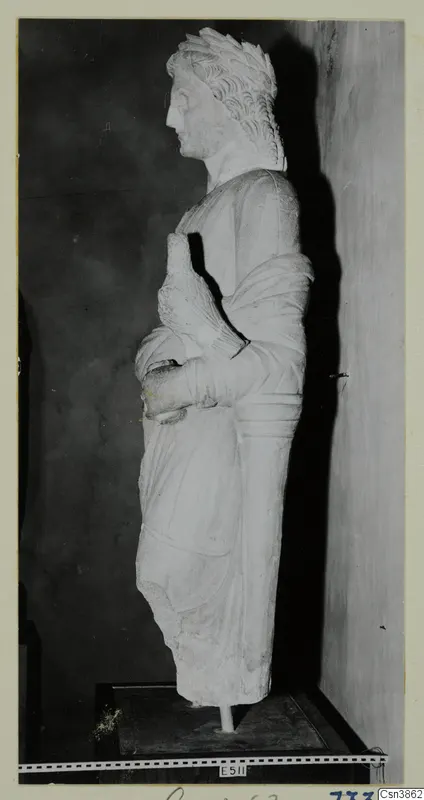 Stone statue of a standing figure in profile, with curled hair and a draped garment, on a dark wooden base.