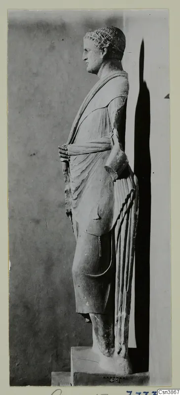 Standing stone statue of a draped figure, seen in side profile against a grey backdrop