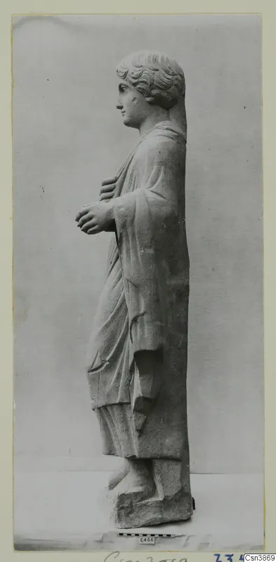 Stone statue of a standing figure in a draped cloak, shown in profile facing left