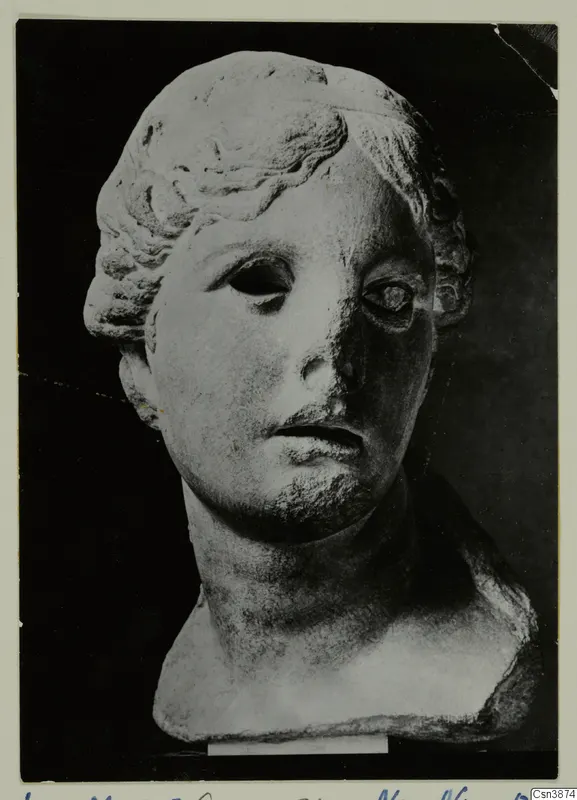 Marble head of a young woman with hair drawn back in waves and a bun, eyes hollow, nose broken.