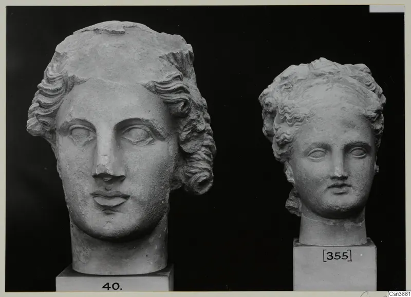 Two sculpted heads with curled, wavy hair, each on a square plinth, shown against a black background.