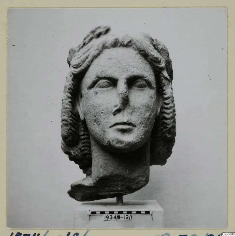 Carved stone head of a woman with wavy hair, set on a short stand in front of a scale bar
