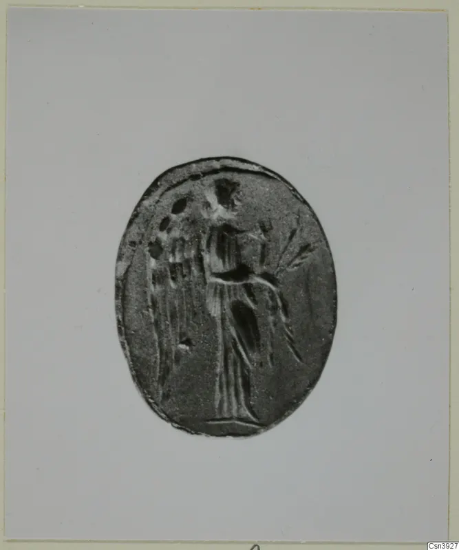 Oval seal or gem engraved with a standing figure in a long garment, photographed on a grey card