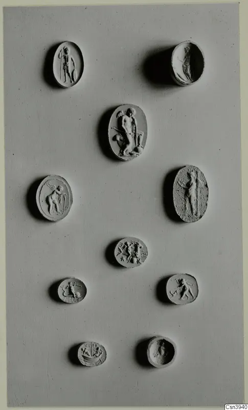 Ten oval seals and gems with engraved or carved figures and animals, arranged on a grey board.