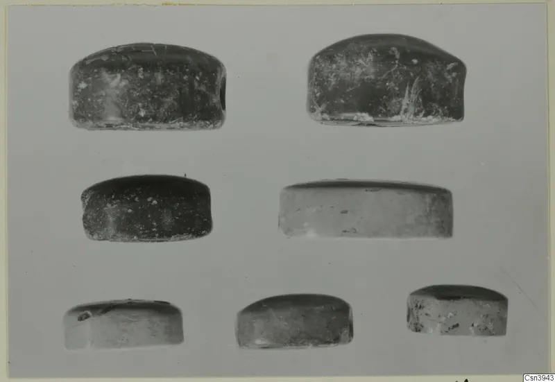 Seven small domed stone objects, dark and pale, arranged in three rows on a grey background, glyptic material