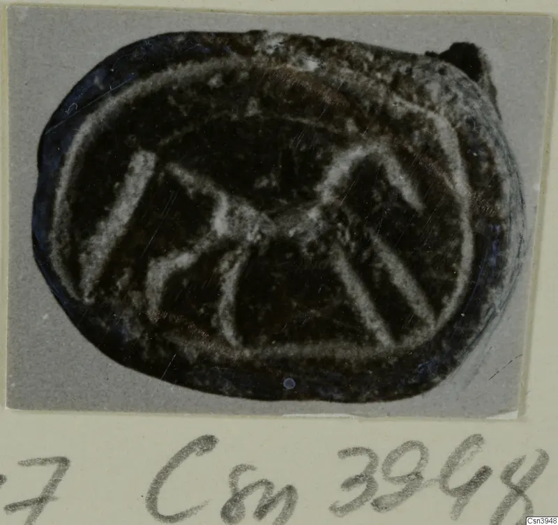 Oval engraved seal of dark stone with a pale incised design, mounted on a grey card